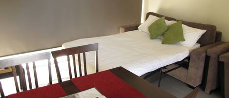 A small, neatly arranged room with a single bed, a table with a red table runner, and two chairs.