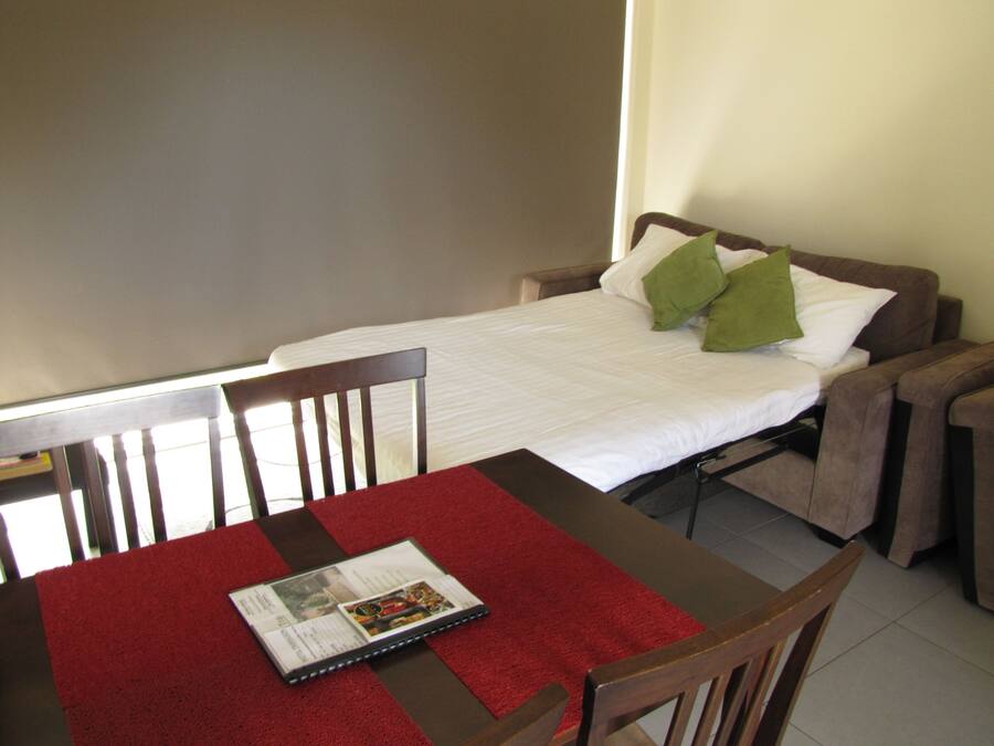 A small, neatly arranged room with a single bed, a table with a red table runner, and two chairs.