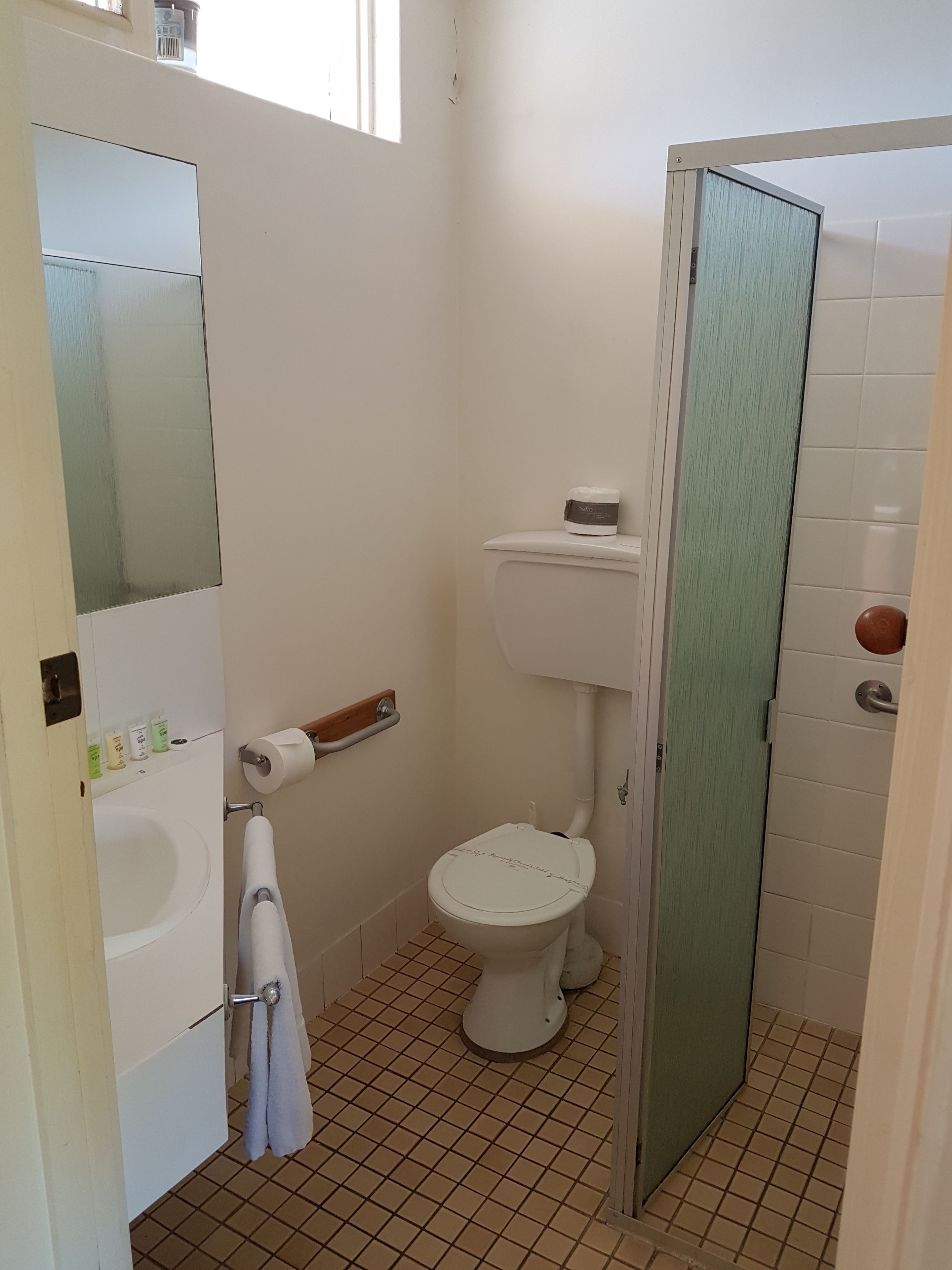 A small, clean bathroom with a toilet, sink, and mirror.