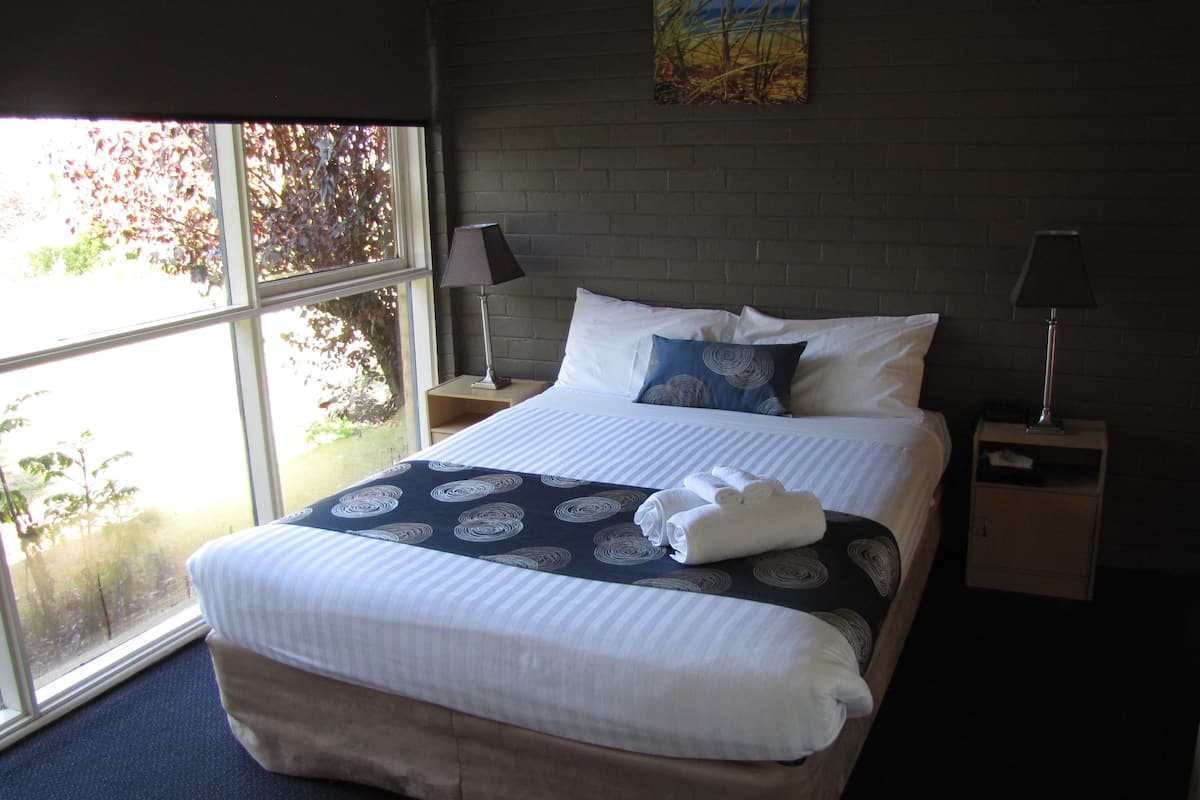 A neatly made bed with a patterned bedspread, two pillows, and a folded towel on a dark blue carpet.