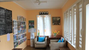 Una habitación acogedora con muebles de mimbre, dispensador de agua y un tablón de anuncios con varios avisos.