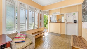 Una habitación acogedora con un sofá de mimbre, un banco de madera y una pequeña mesa. Hay ventanas con vidrio esmerilado y una puerta con un cartel de 'Welcome'.