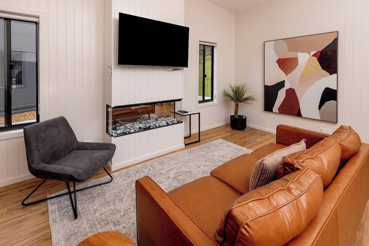 Een moderne woonkamer met een flatscreen televisie, een open haard, een bank en een fauteuil.