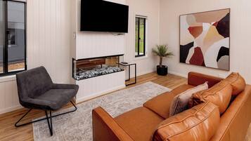A modern living room with a flat-screen TV, a fireplace, a sofa, and a chair.