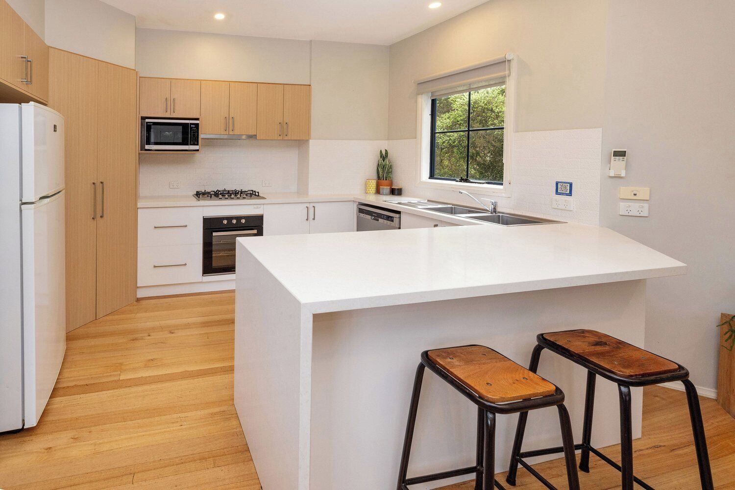 A modern kitchen with a central island, wooden cabinets, a microwave, stove, and a window with a view.