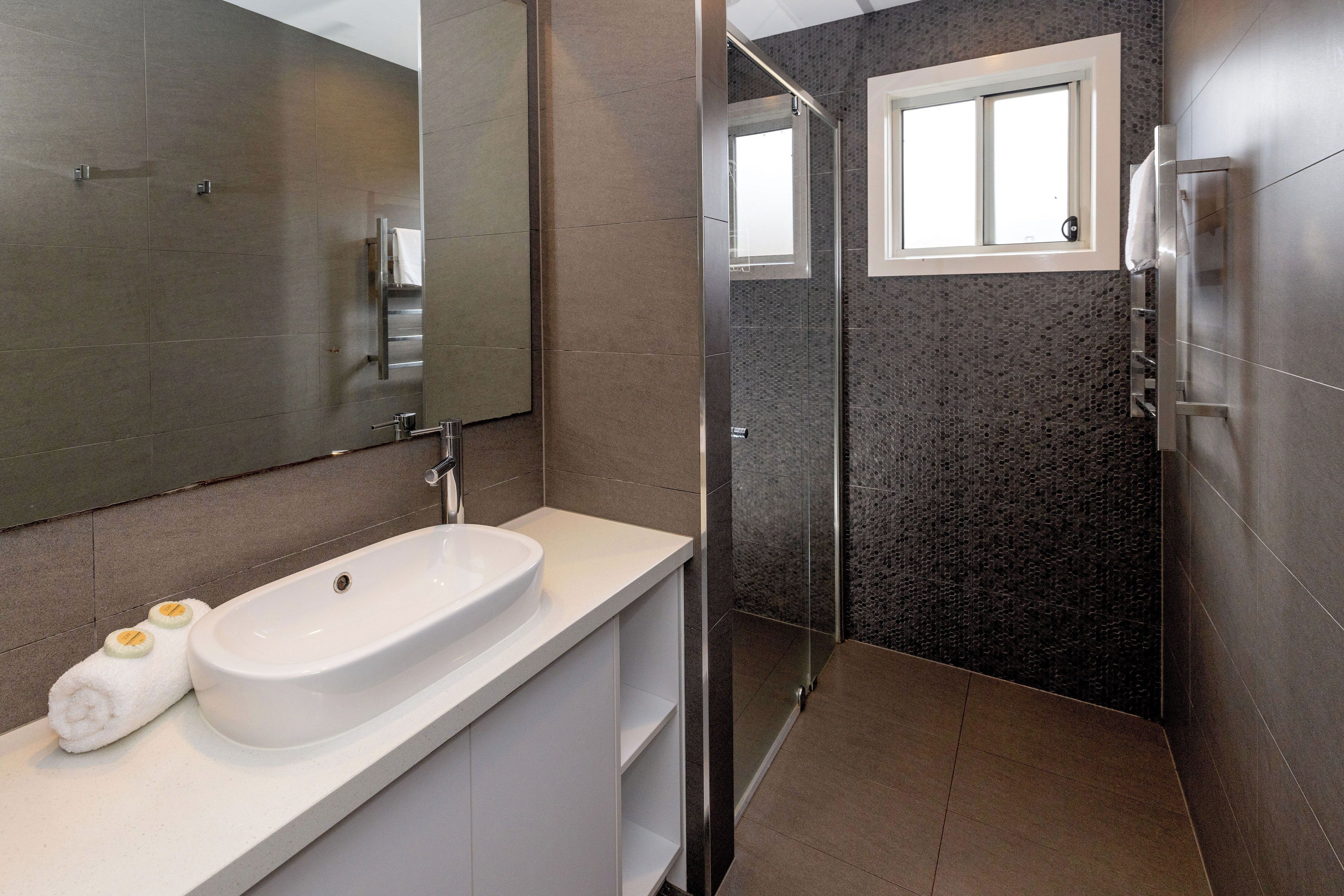 Een moderne badkamer met een witte wastafel, een douchecabine van glas en een klein raam.