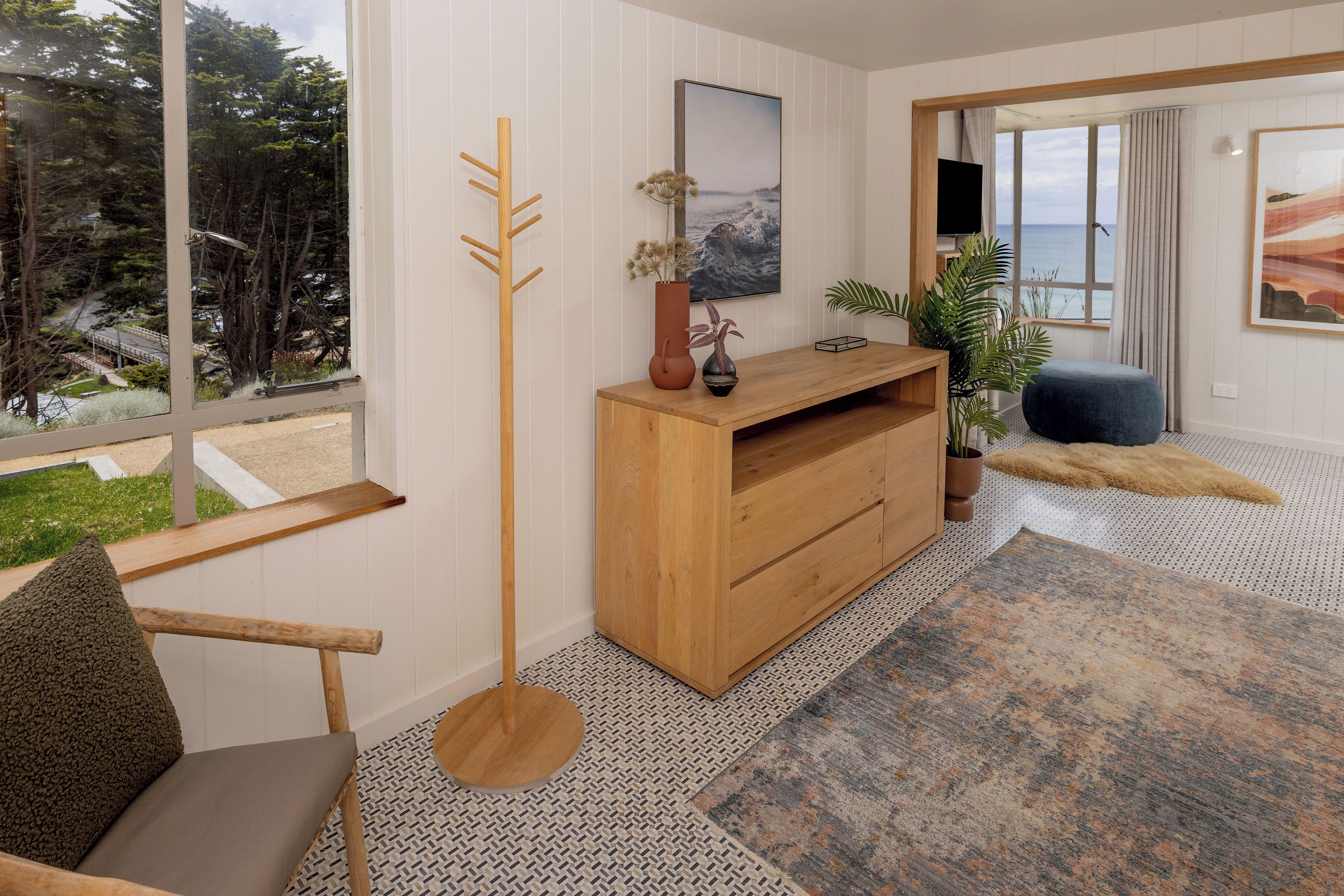 A modern living room with a wooden console table, a floor lamp, a sofa, and a view of the outdoors through large windows.