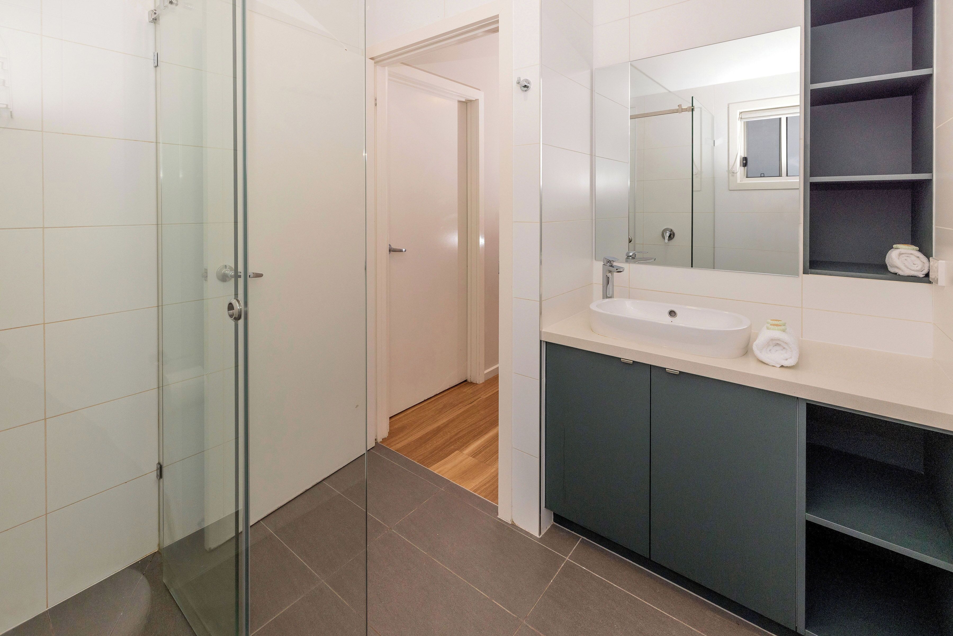 Uma casa de banho moderna com cabine de duche em vidro, uma pia com espelho e uma toalha no balcão.