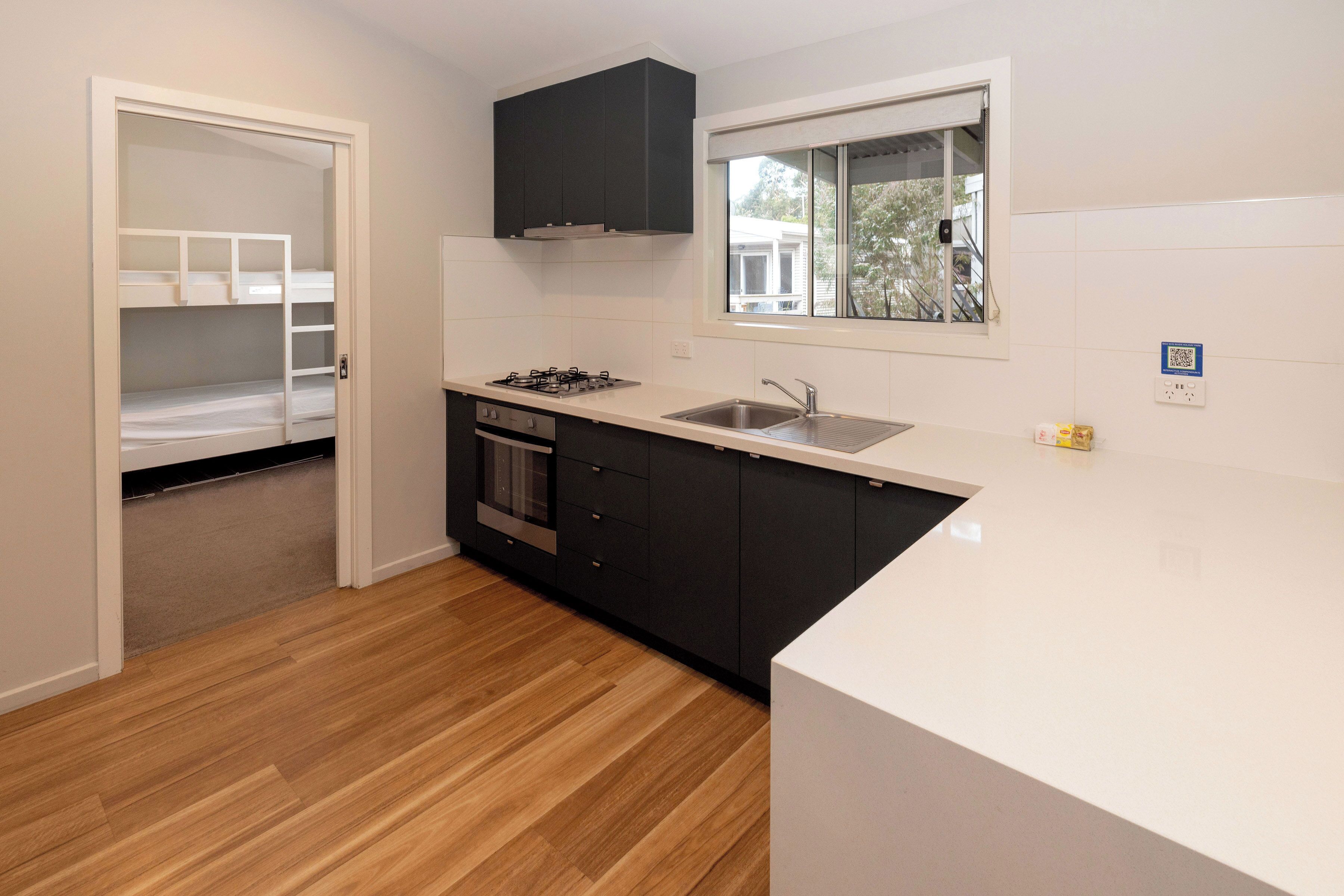 A kitchen with a white countertop, black cabinets, a window, and a door leading to a bedroom.