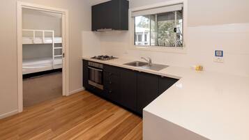 A kitchen with a white countertop, black cabinets, a window, and a door leading to a bedroom.