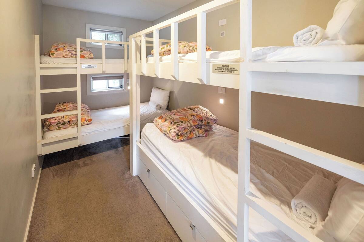 Een slaapkamer met stapelbed, een raam, vloerbedekking en een witte muur.