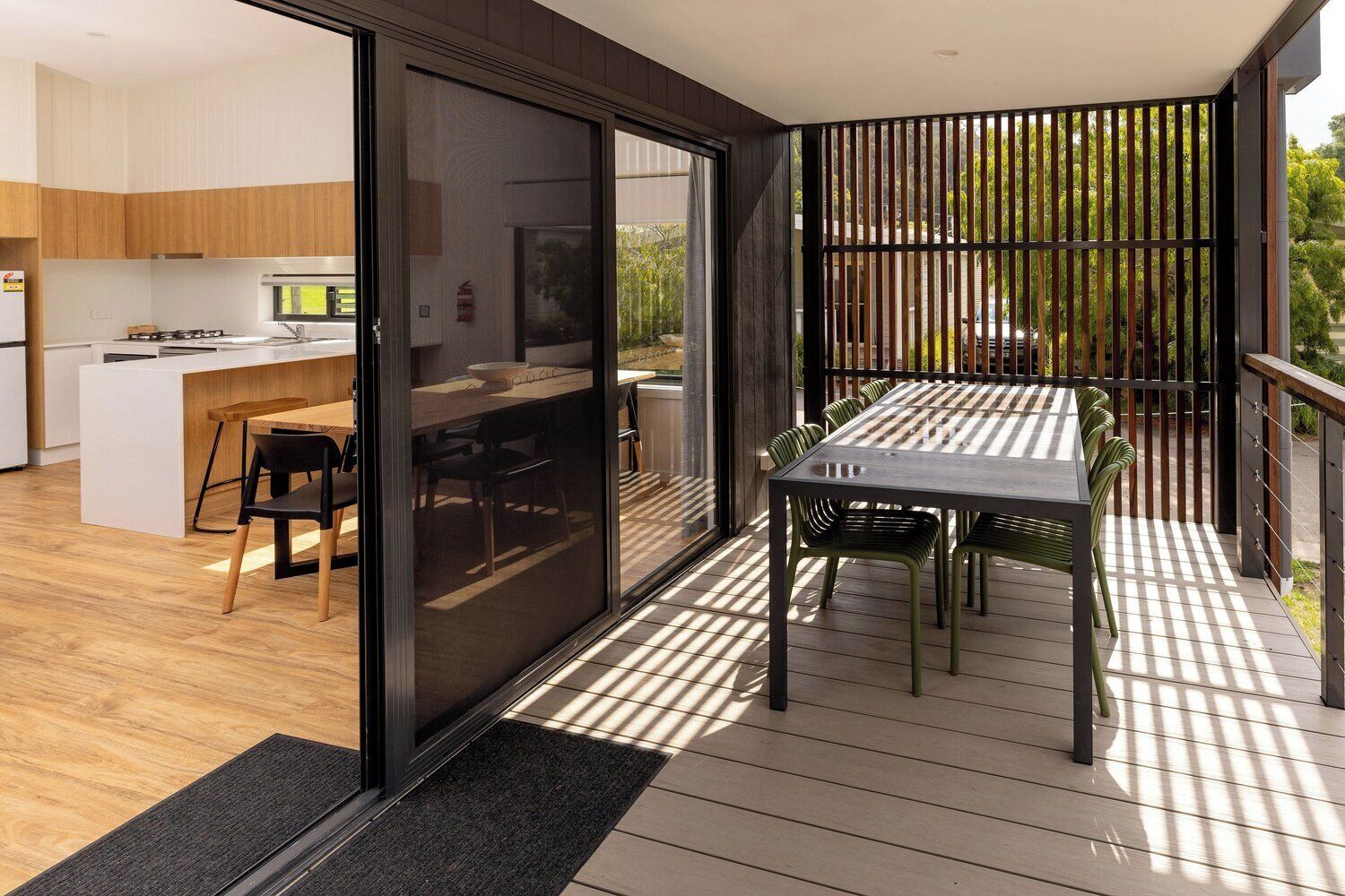 A modern kitchen with a central island, a dining area with a table and chairs, and a balcony with a railing.