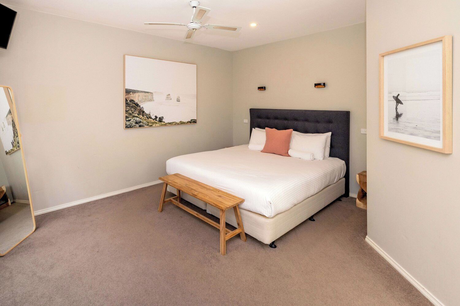 A bedroom with a bed, a bench, a ceiling fan, and two framed pictures on the walls.