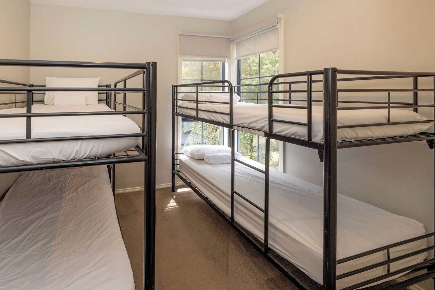 Habitación tipo dormitorio con literas, ventana con vista a árboles y suelo alfombrado.