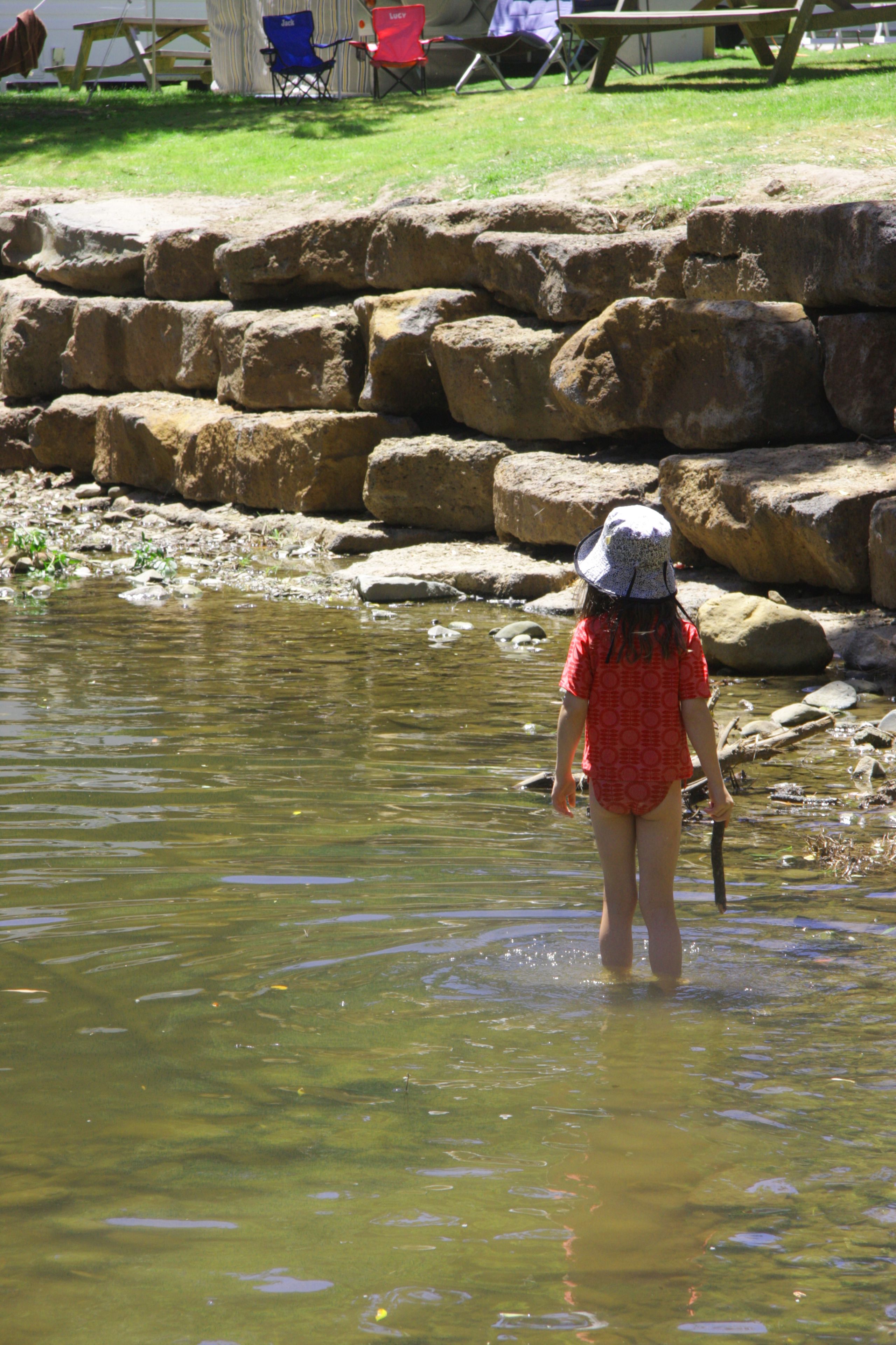 A person wading in a shallow body of water with rocks and a picnic table in the background.