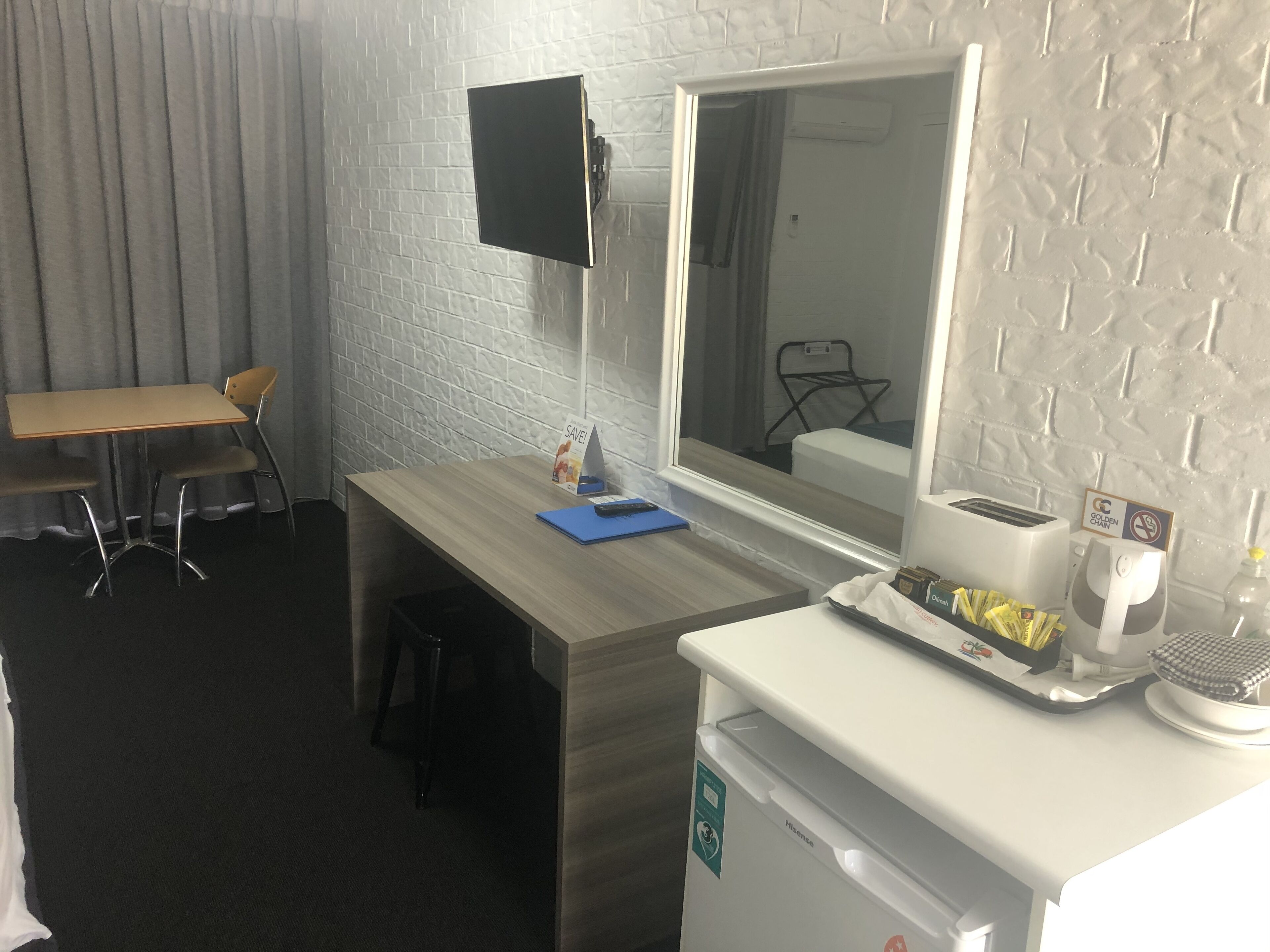Habitación de hotel con escritorio de madera, una silla, refrigerador pequeño, microondas, ventana y televisor montado en la pared.