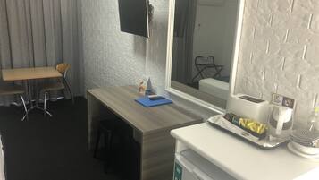 Habitación de hotel con escritorio de madera, una silla, refrigerador pequeño, microondas, ventana y televisor montado en la pared.