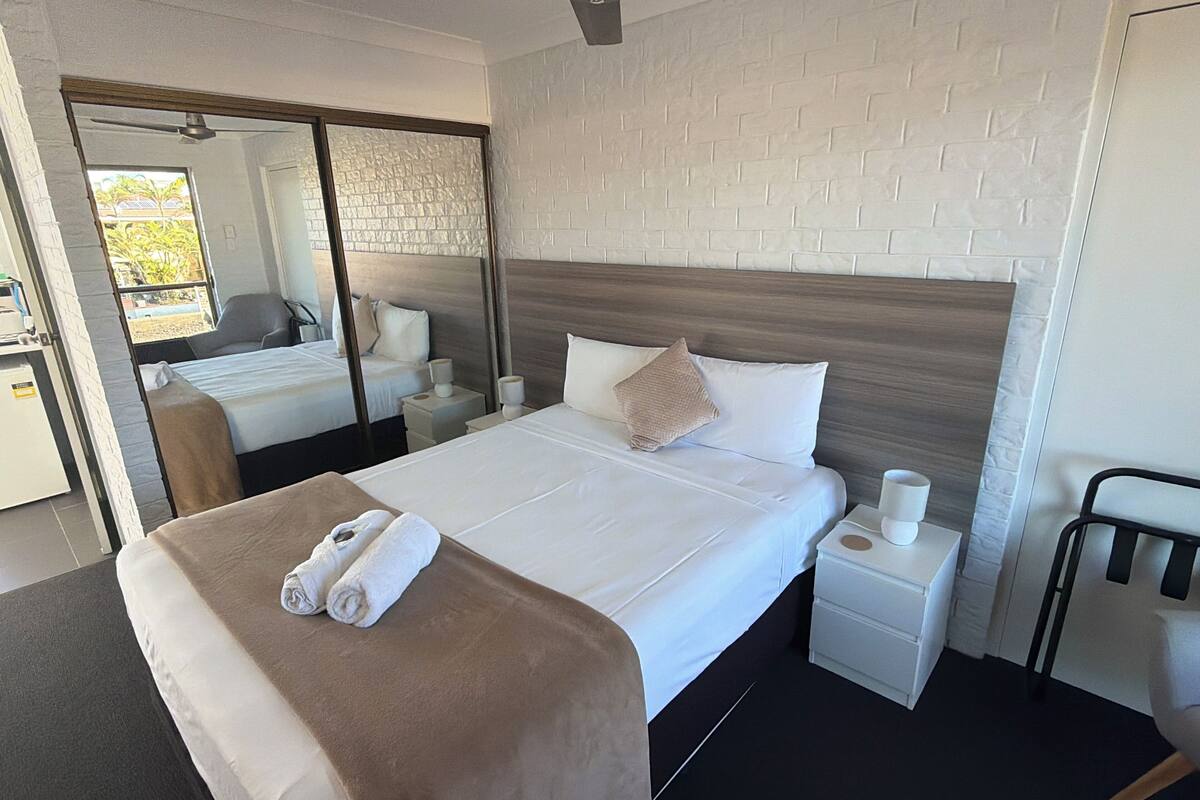 A hotel room with a large bed, a bedside table with a lamp, a mirror, and a ceiling fan.