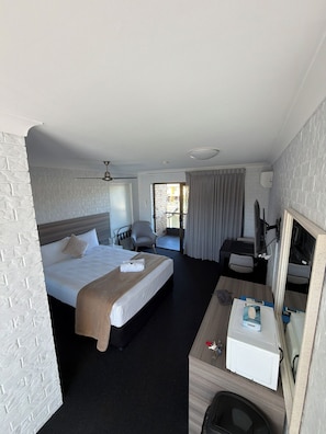 Quarto de hotel com cama, escrivaninha, cadeira, televisão e janela.