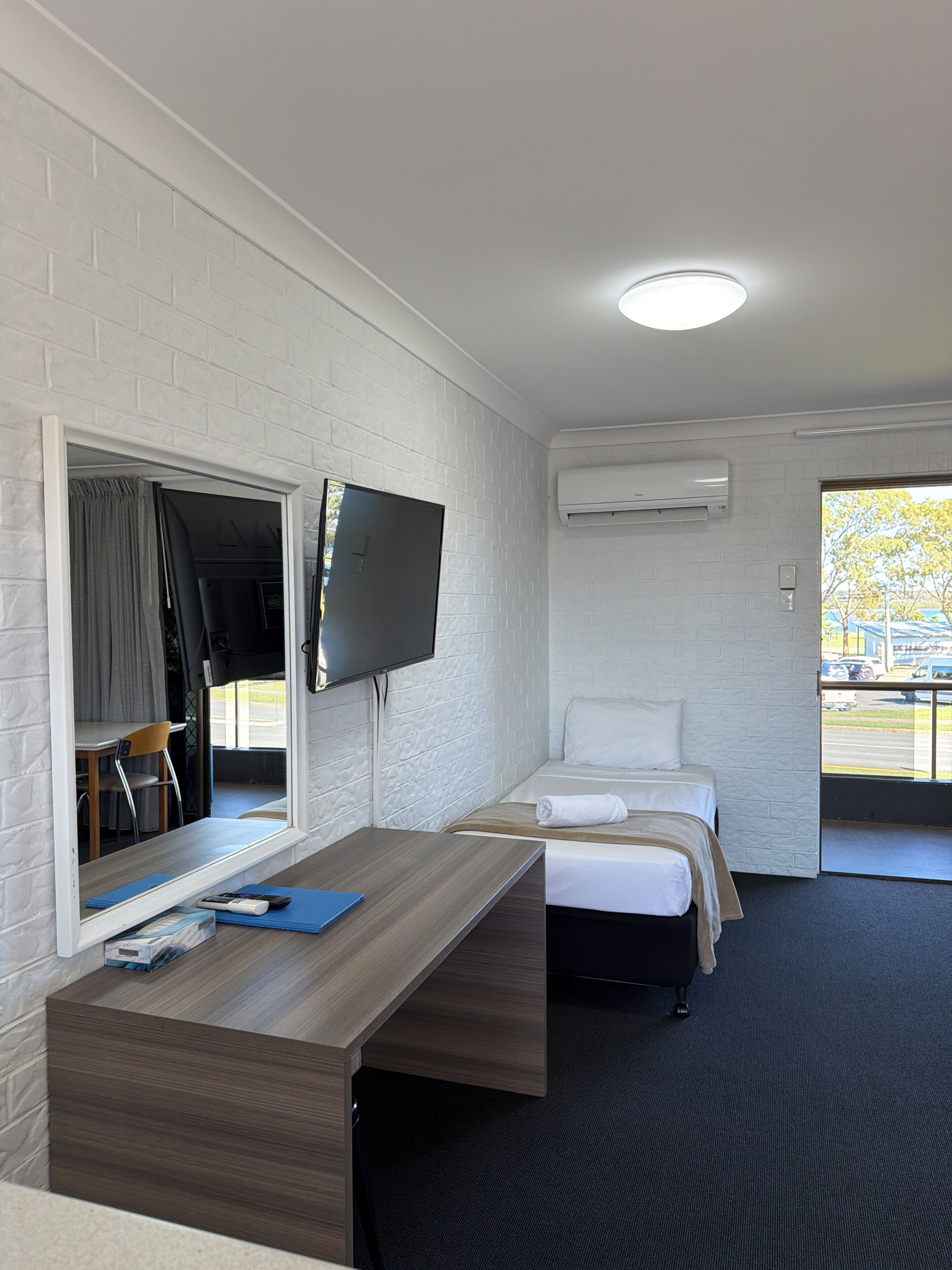 Une chambre d’hôtel équipée d’un lit, d’un bureau avec un ordinateur, d’un téléviseur fixé au mur et d’un appareil de climatisation.