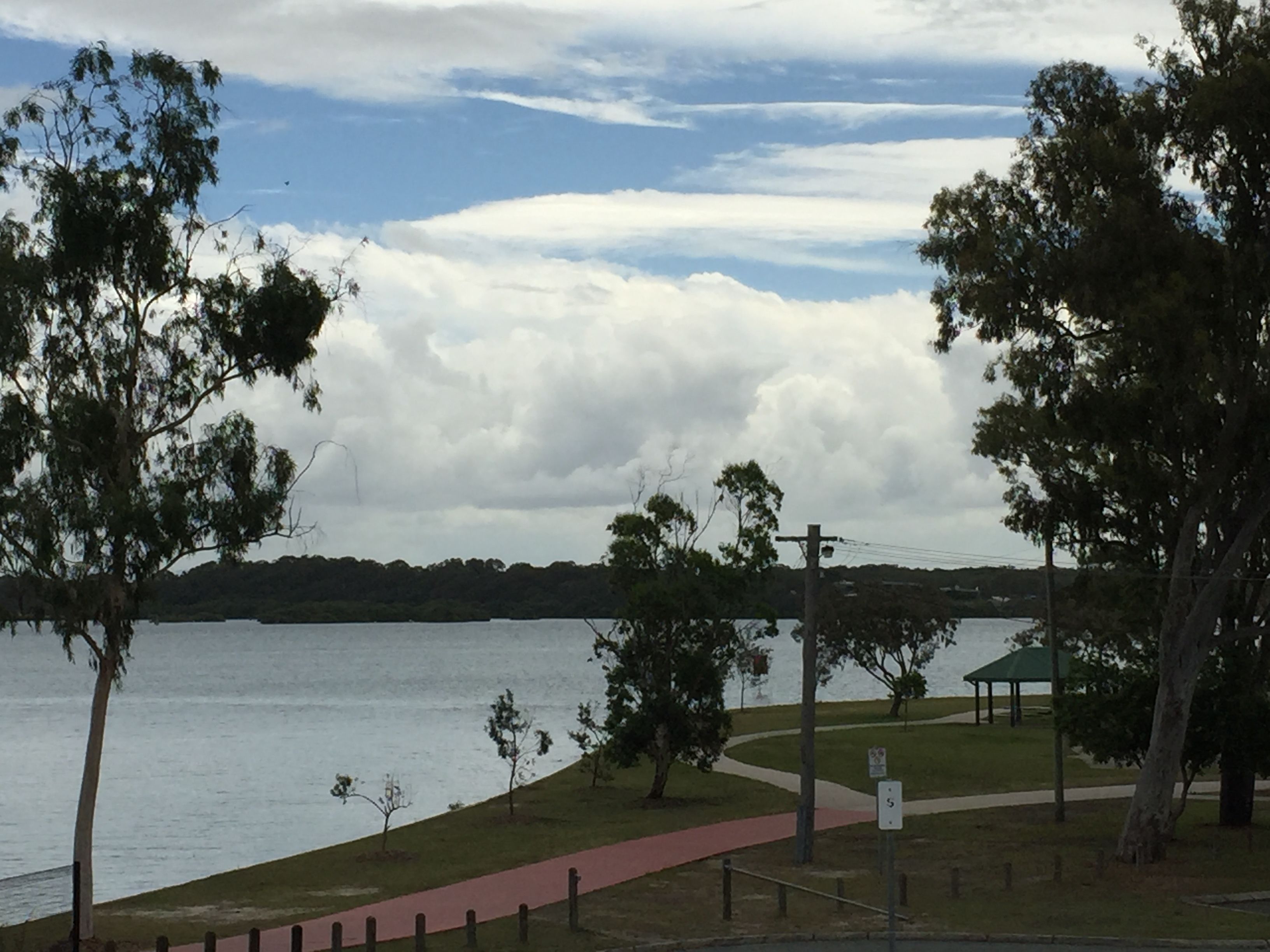 A lakeside park with a walking path, trees, and a gazebo.