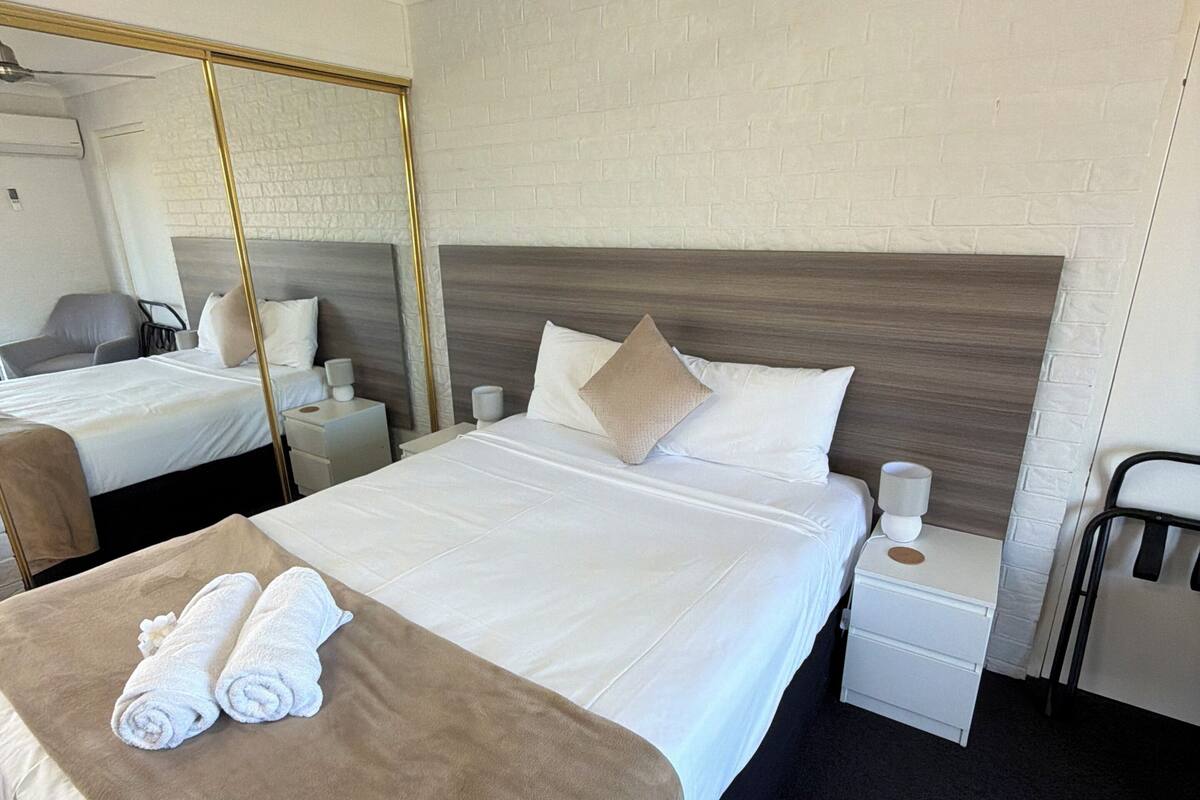A hotel room with a large bed, a bedside table with a lamp, a ceiling fan, and a mirror.