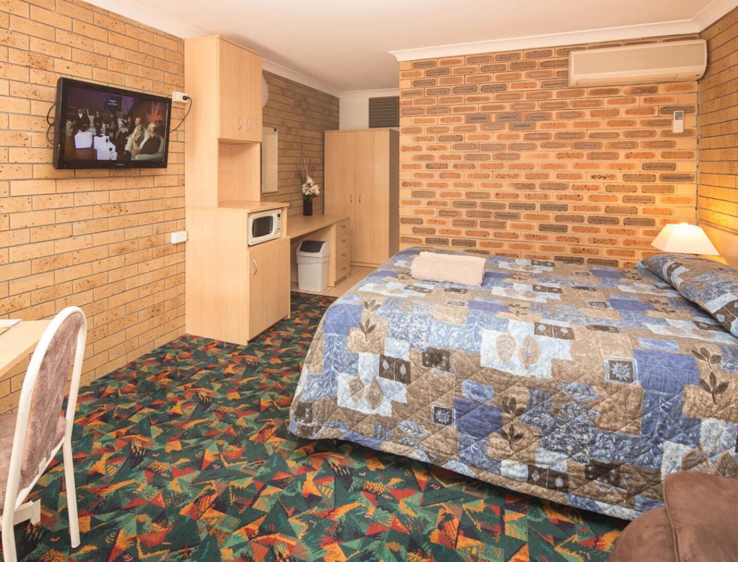 Een hotelkamer met een bed, een bureau, een televisie en een bakstenen muur.