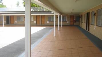 A corridor with a tiled floor, white pillars, and a covered area with windows.