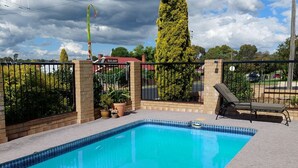 A rectangular swimming pool with a tiled edge, surrounded by a brick wall and a metal fence. - Settlers Motor Inn (Tenterfield)