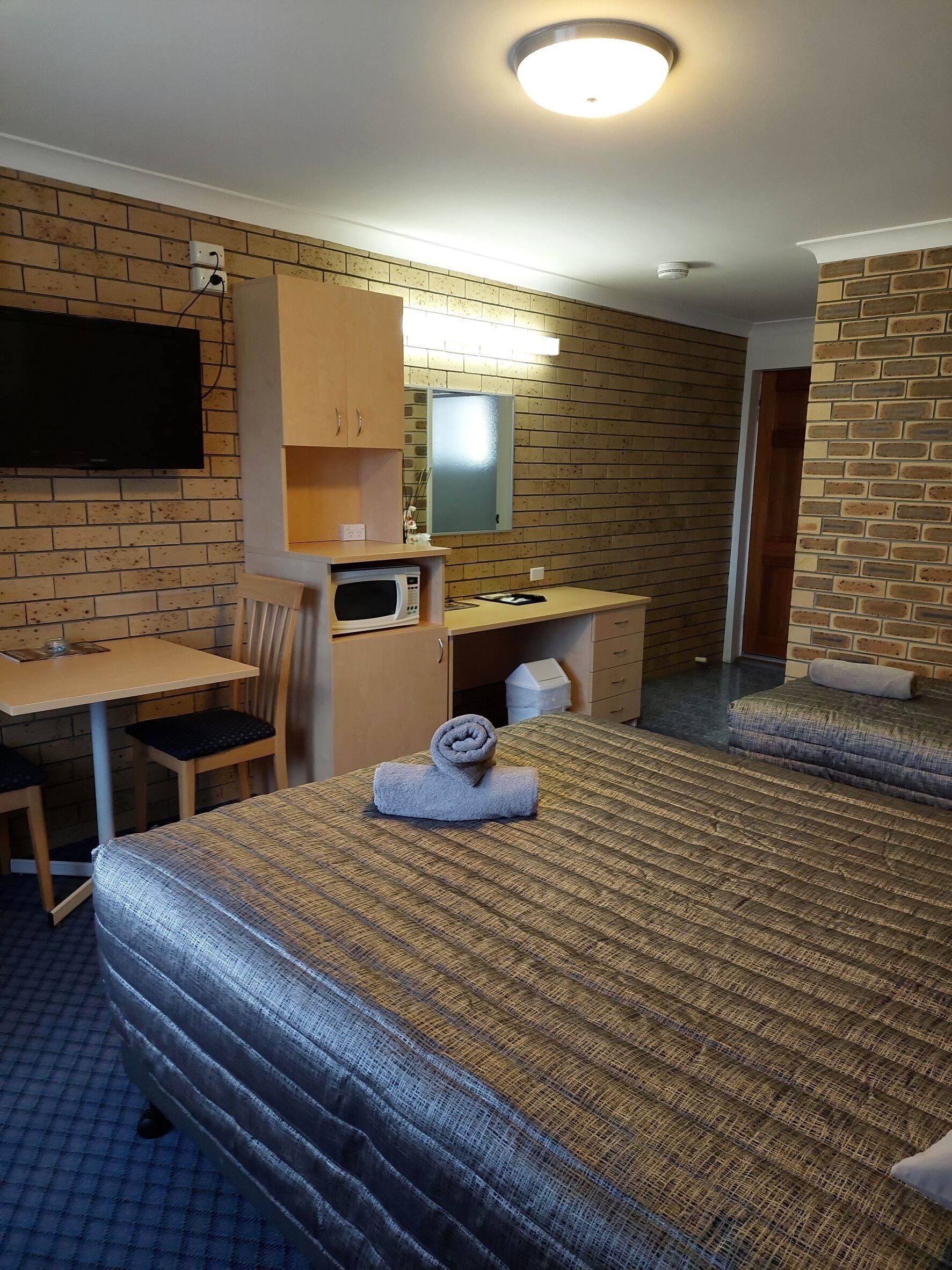 Una habitación de hotel con dos camas, un escritorio, una silla, un televisor y un microondas.