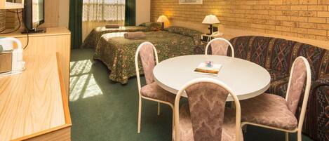 Una habitación con pared de ladrillo, una cama, un sofá, una mesa de comedor con sillas y un televisor.