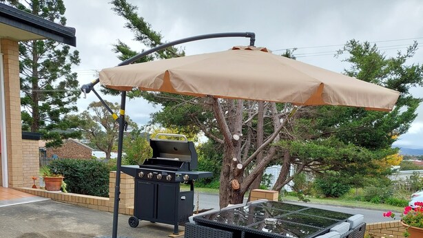 An outdoor patio with a grill, wicker furniture, and a large umbrella.