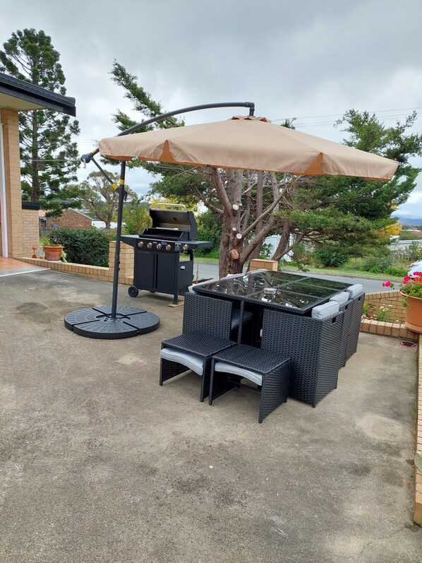 An outdoor patio with a grill, wicker furniture, and a large umbrella.