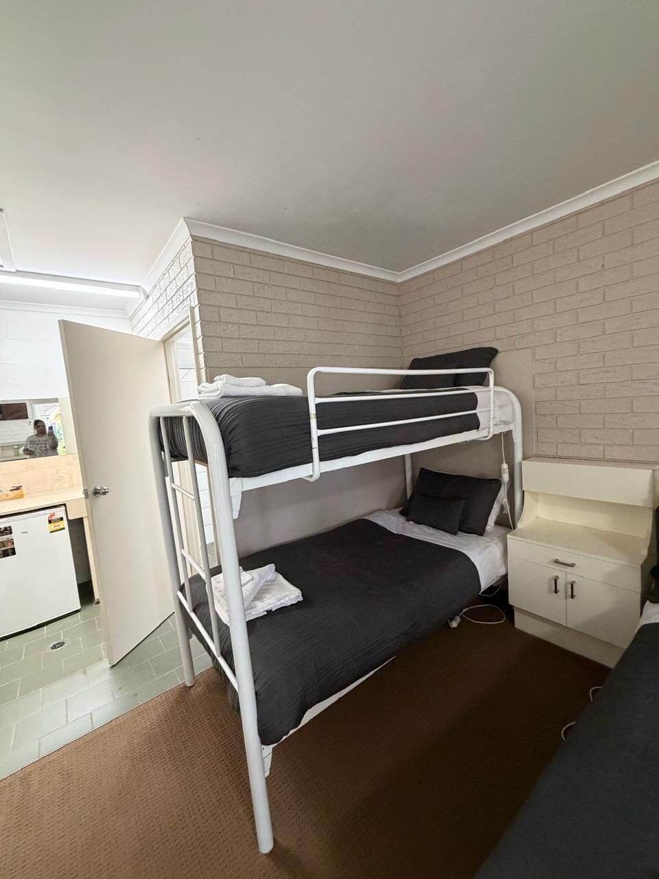 Quarto com beliche, escrivaninha, um pequeno armário e porta que dá para outro cômodo.