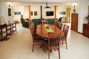 A dining area with a wooden table and chairs, a sofa, and a television mounted on the wall.
