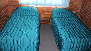 A room with two single beds, a wooden nightstand, and a window with sheer curtains.