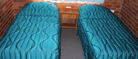 A room with two single beds, a wooden nightstand, and a window with sheer curtains.