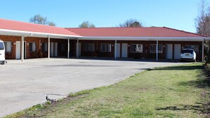 A motel with a red-tiled roof, a covered parking area, and a grassy lawn.