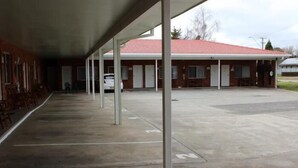 A motel with a covered parking area, a red-tiled roof, and a row of rooms with windows.