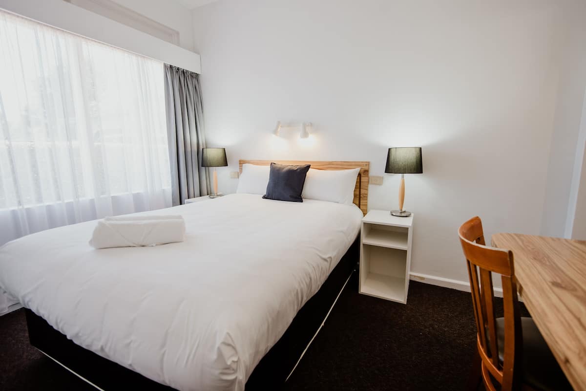 A hotel room with a large bed, bedside lamps, a wooden nightstand, a wooden chair, and a small table.