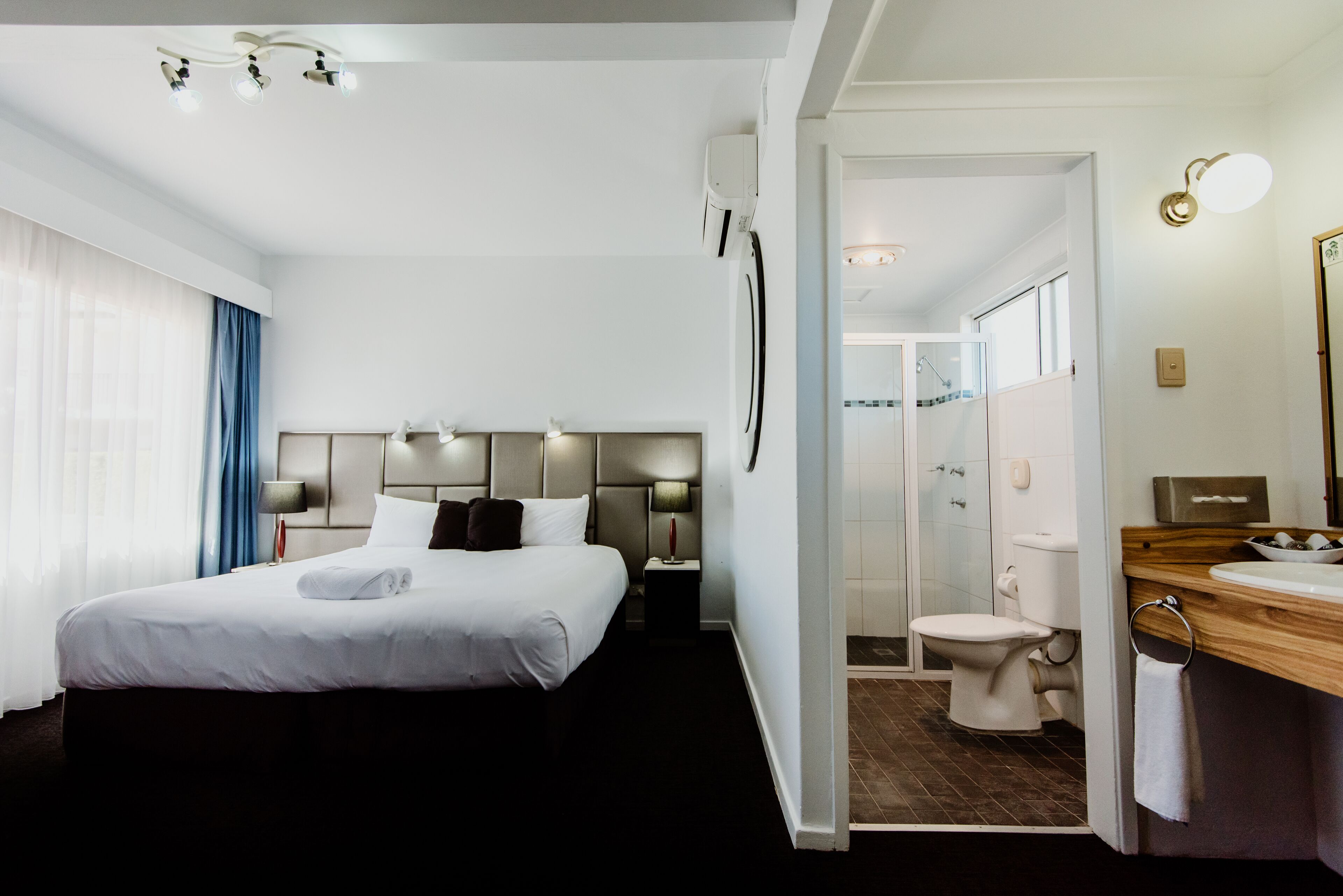 A hotel room with a large bed, bedside lamps, a bathroom with a toilet and sink, and a shower area.