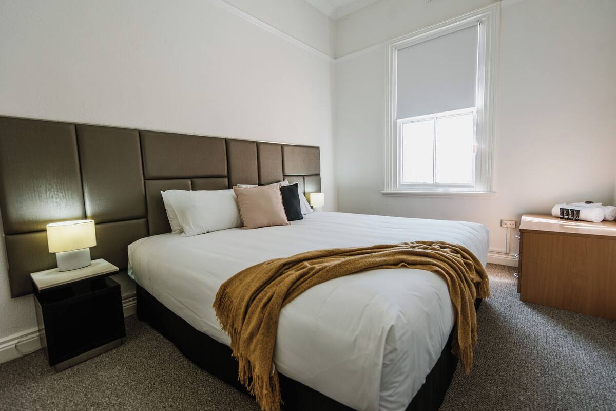 A bedroom with a bed, nightstand, bedside lamp, and a window.