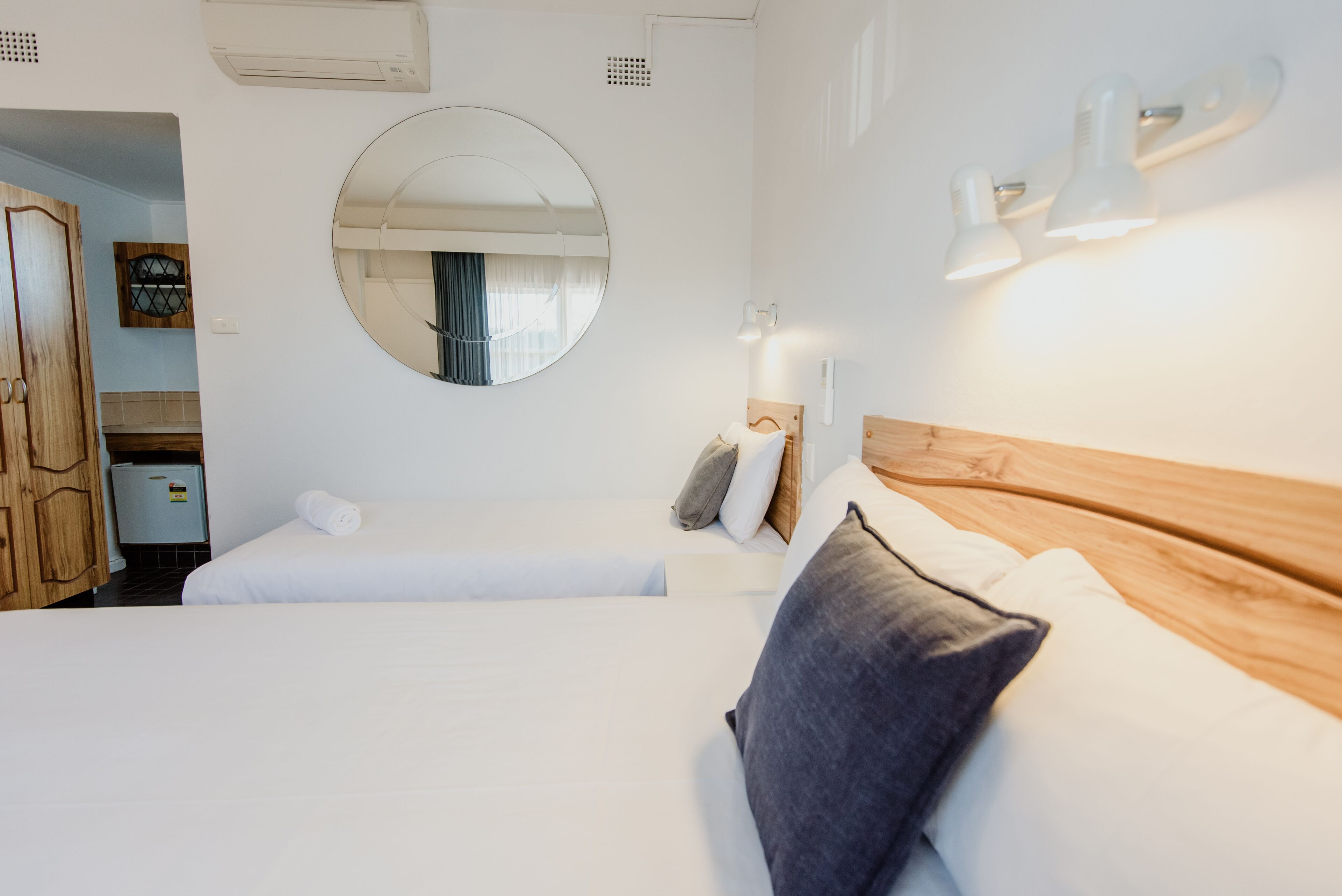 A hotel room with two beds, a round mirror, wall-mounted lights, and a wooden headboard.