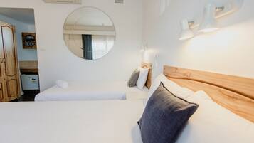 A hotel room with two beds, a round mirror, wall-mounted lights, and a wooden headboard.