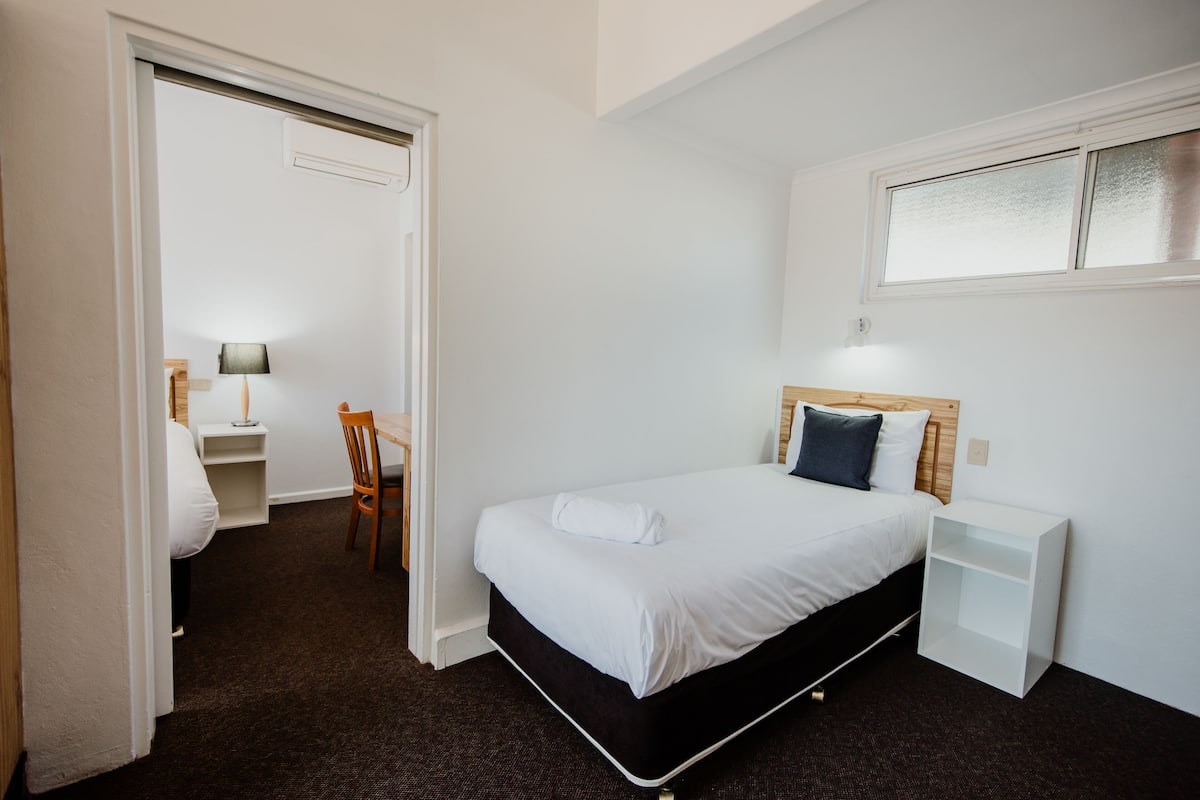 A hotel room with a bed, a bedside table, a chair, a desk, and a window.