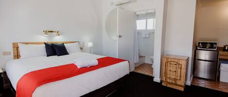 Une chambre d’hôtel avec un grand lit, une petite kitchenette, un appareil de climatisation et une salle de bain visible à travers une porte ouverte.