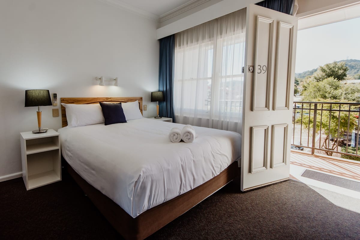 A hotel room with a large bed, a wooden headboard, a nightstand with a lamp, a view of the outdoors through a balcony door, and a number 39 on the door.