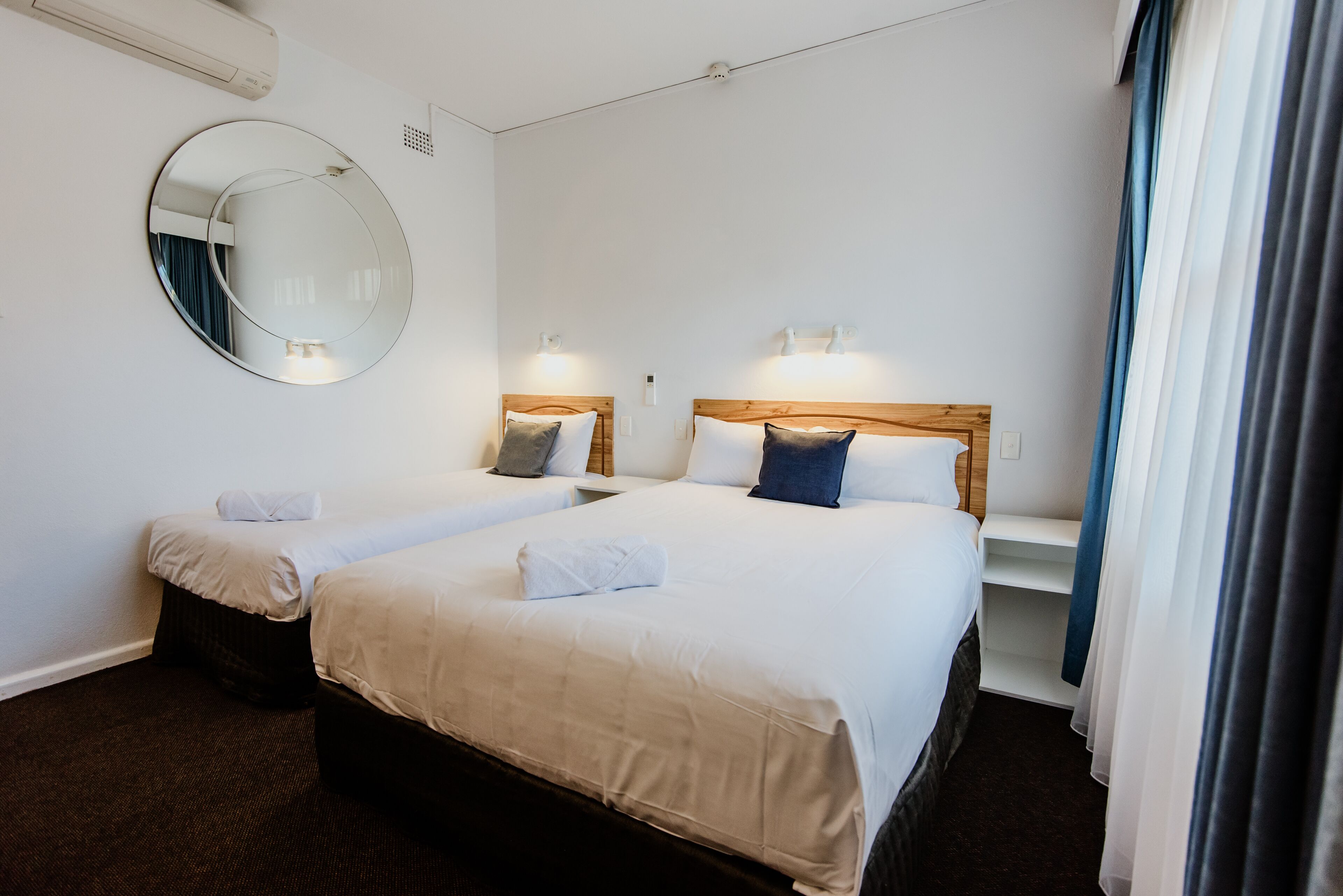 Une chambre d’hôtel avec deux lits, un miroir rond et des lampes de chevet.