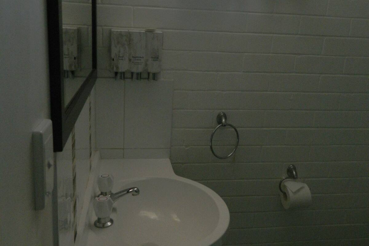 Un baño con lavamanos blanco, espejo, toallero y dispensador de papel higiénico.