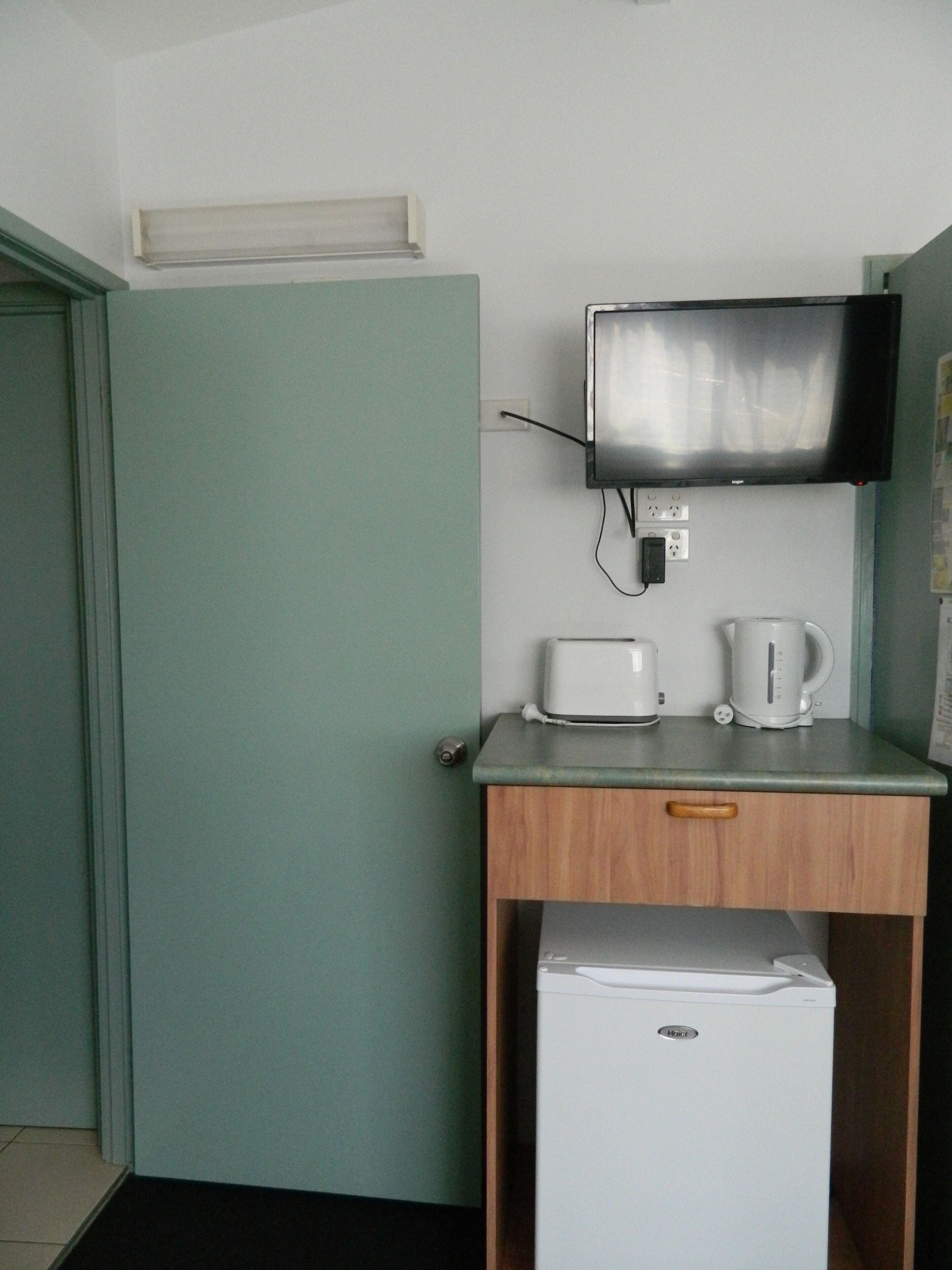 A kitchenette with a microwave, toaster, and coffee maker on a counter, a small refrigerator, and a television mounted on the wall.